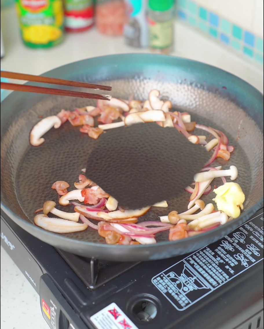 Un trozo de mantequilla derritiéndose en la mezcla de tocino, champiñones y cebolla.