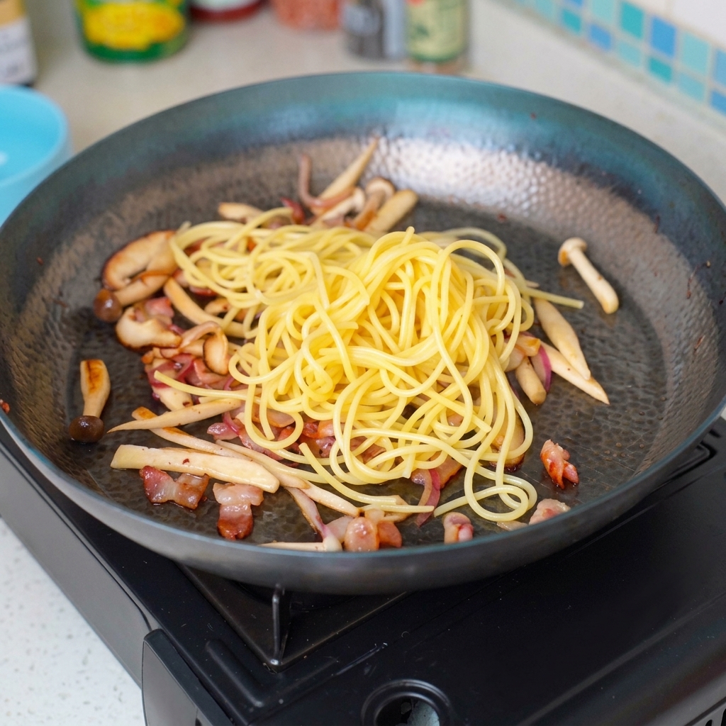 Pasta cabello de ángel mezclándose con los ingredientes salteados en la sartén.