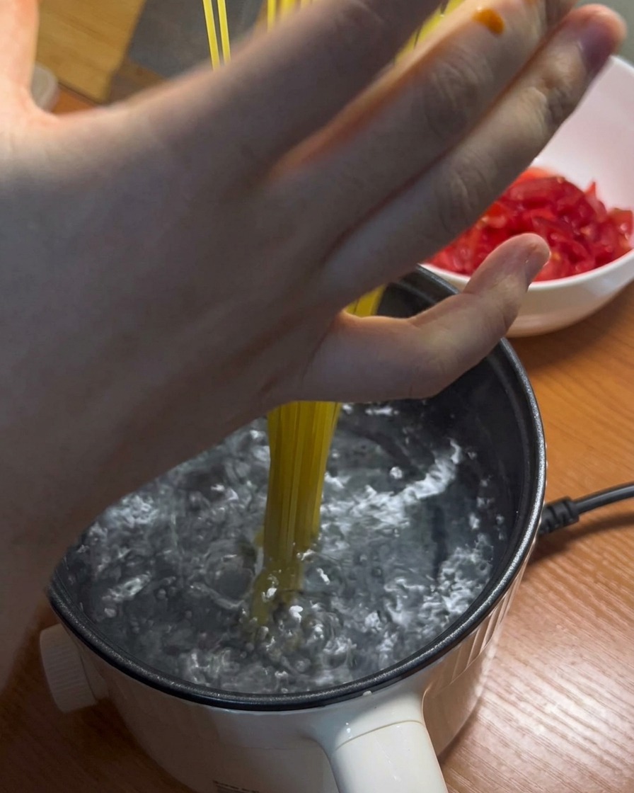 Fideos largos de espaguetis siendo añadidos a una olla de agua hirviendo.