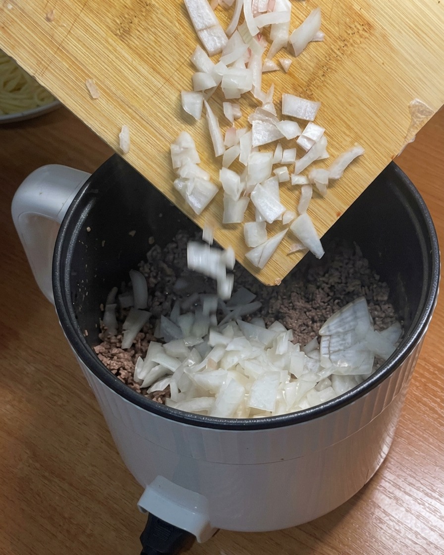 Cebolla picada siendo añadida a la olla que contiene la carne picada dorada.