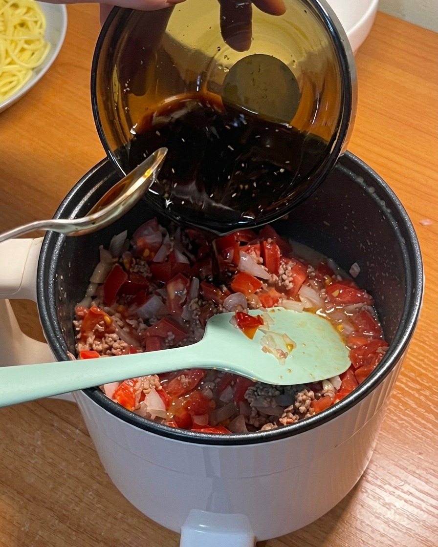 Salsa de condimentos oscura siendo vertida desde un cuenco a la olla con los tomates, la carne y la cebolla.