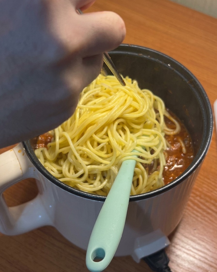 Espaguetis cocinados siendo añadidos a la salsa de tomate y carne a fuego lento.
