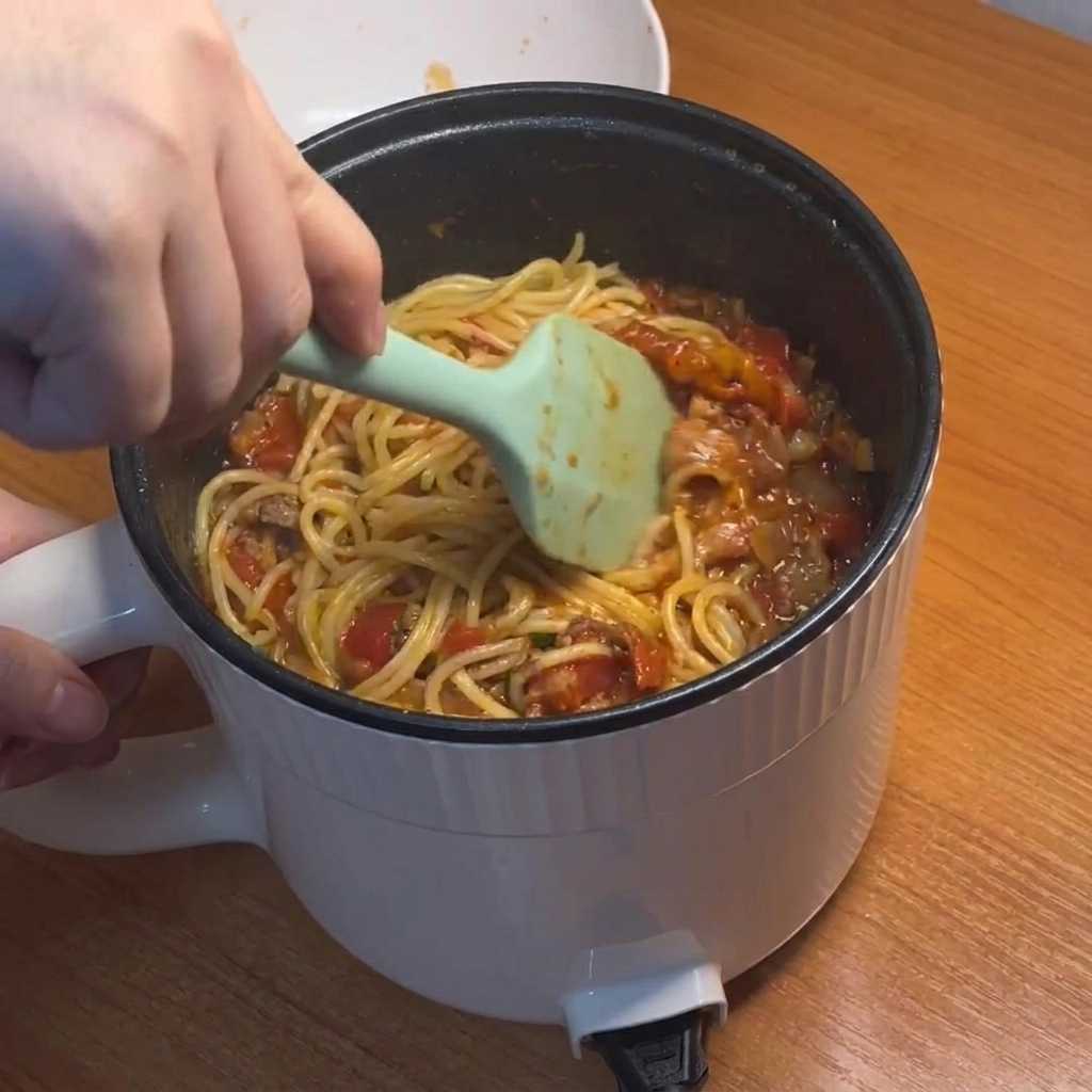 Espaguetis siendo removidos y cubiertos con la espesa salsa roja de tomate y carne.