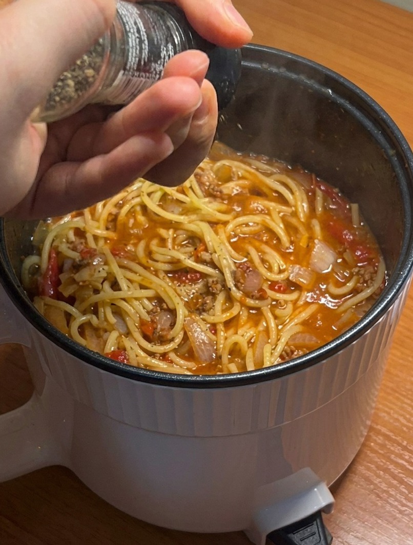 Primer plano de una olla de espaguetis terminados con salsa de carne, sazonados con pimienta negra recién molida.