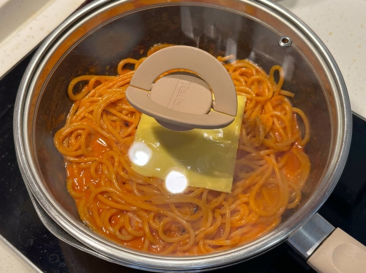 Una sartén con espaguetis cubiertos con una loncha de queso y una tapa de cristal.