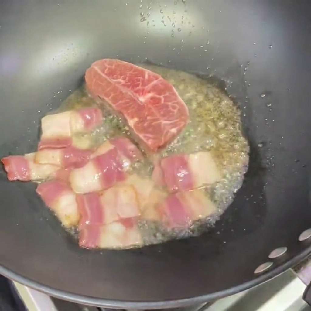 Dos filetes pequeños friéndose en un wok junto a los trozos de tocino.