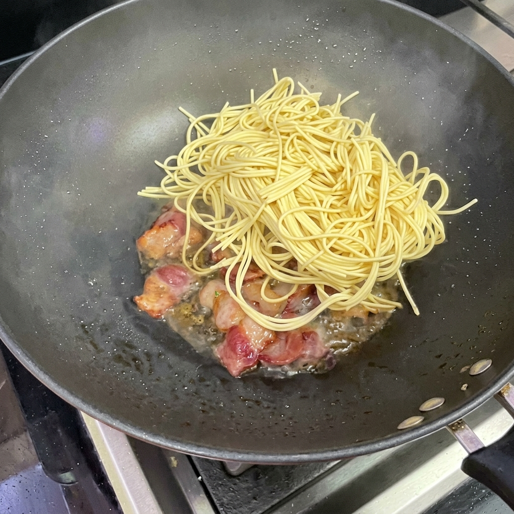 Espaguetis siendo añadidos al wok con tocino.