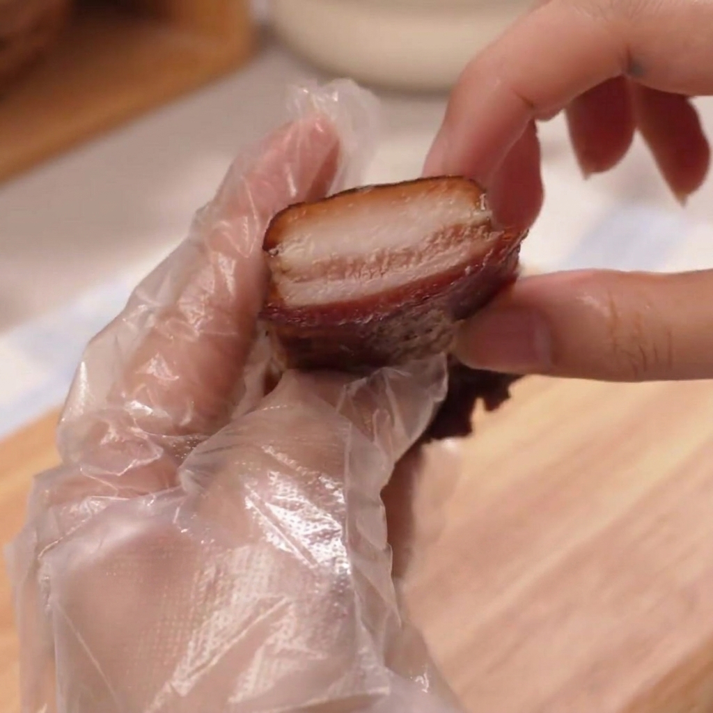 Una mano con guante sosteniendo una rebanada de jamón grueso.