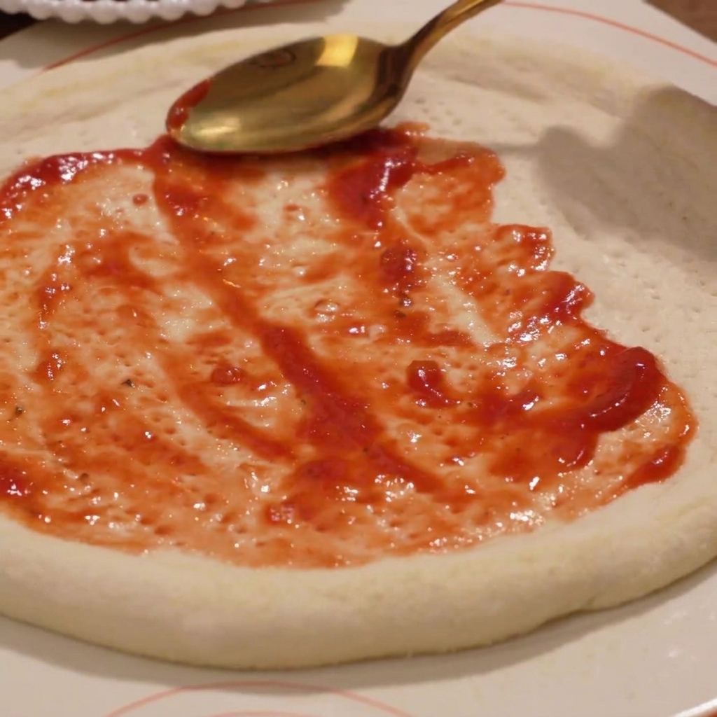 Esparciendo salsa de tomate sobre la base de pizza.