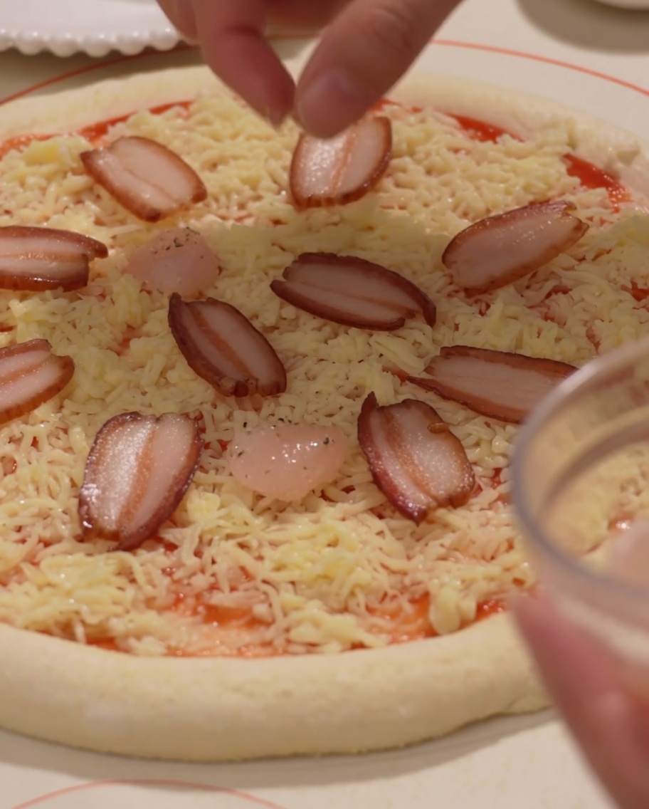 Colocando jamón y camarones sobre la base de pizza con queso.