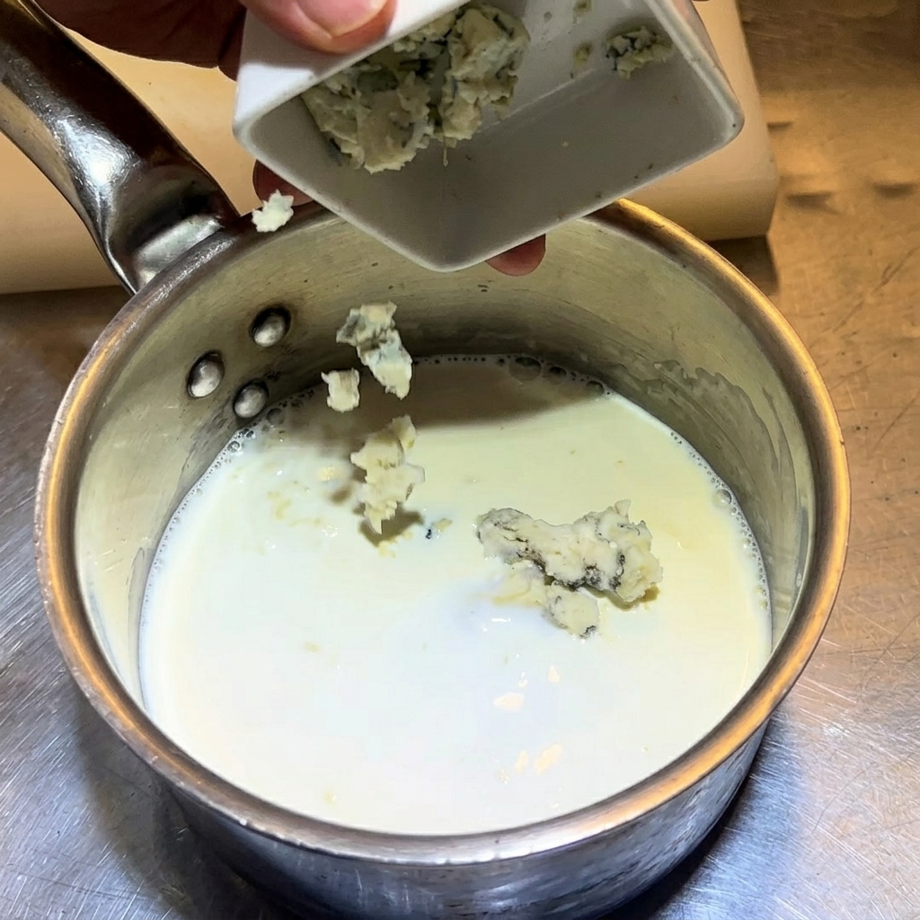 Dejando caer trozos de queso azul desmenuzado en una cacerola con leche y crema.