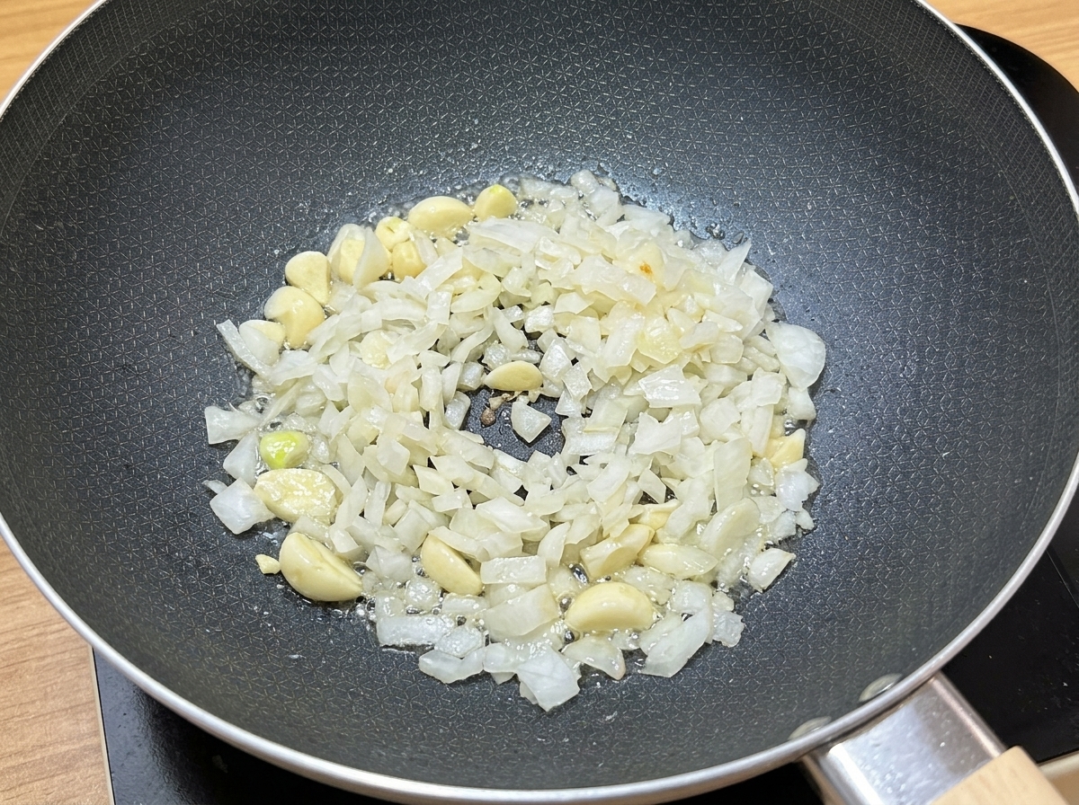 Ajo picado y cebolla troceada friéndose en aceite caliente en una sartén oscura.