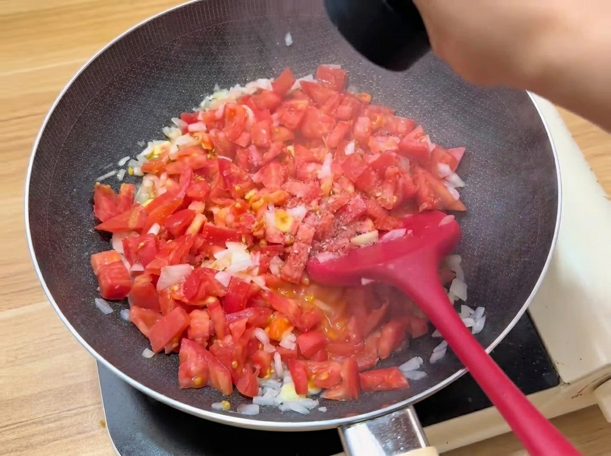 Tomates troceados cocinándose en una sartén con condimentos.