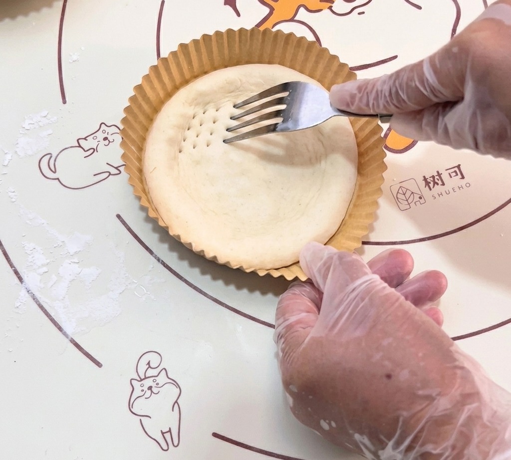 Un tenedor creando pequeñas hendiduras en la base de masa cruda.
