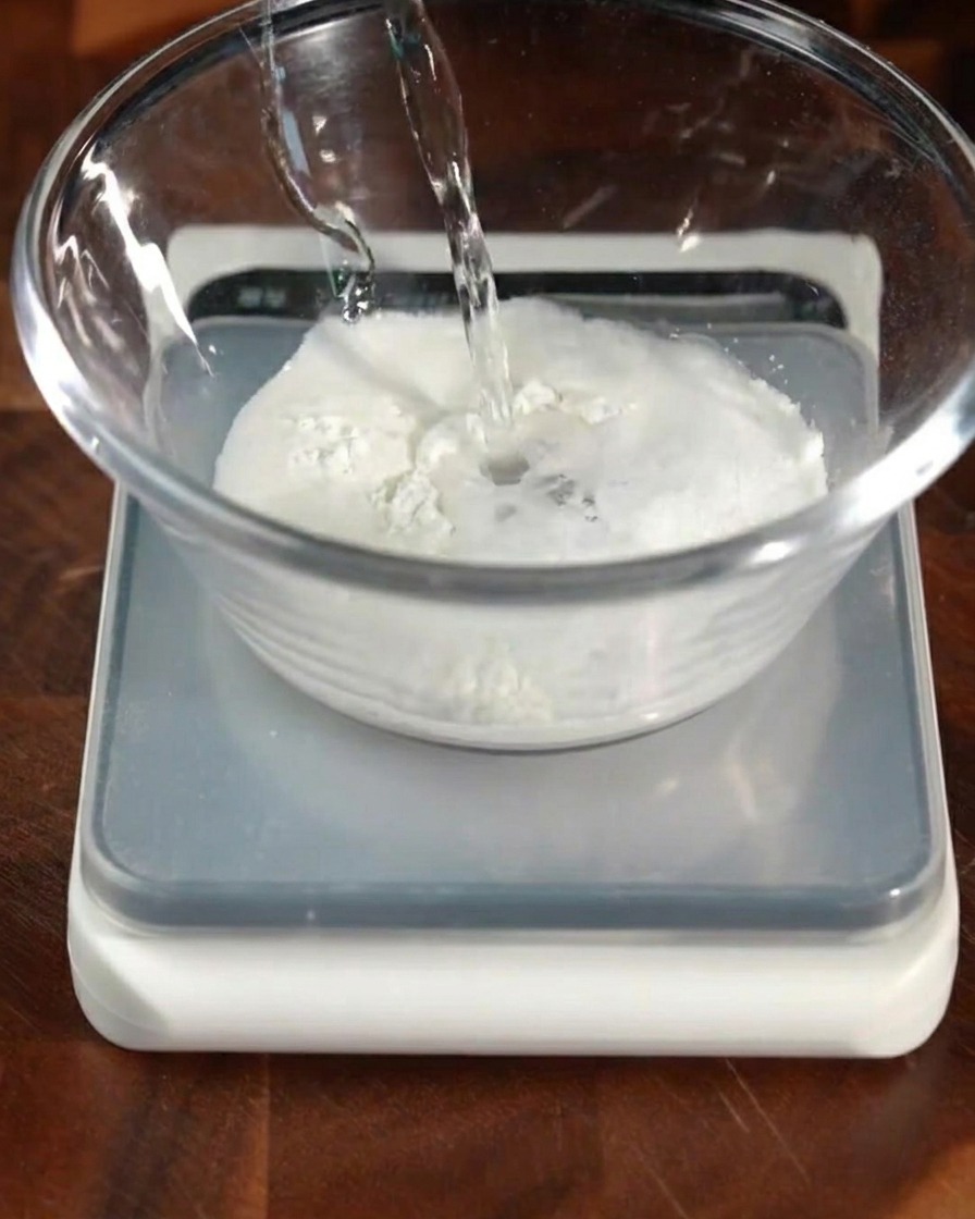 Agua tibia con levadura siendo vertida en un bol con harina y otros ingredientes secos.