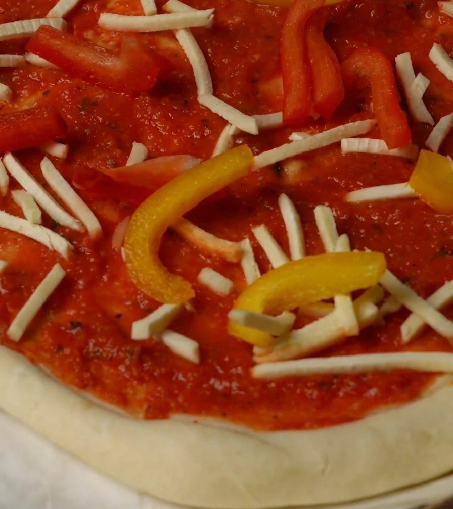 Pizza cubierta con pimientos, queso y trozos de langosta, lista para el horno.