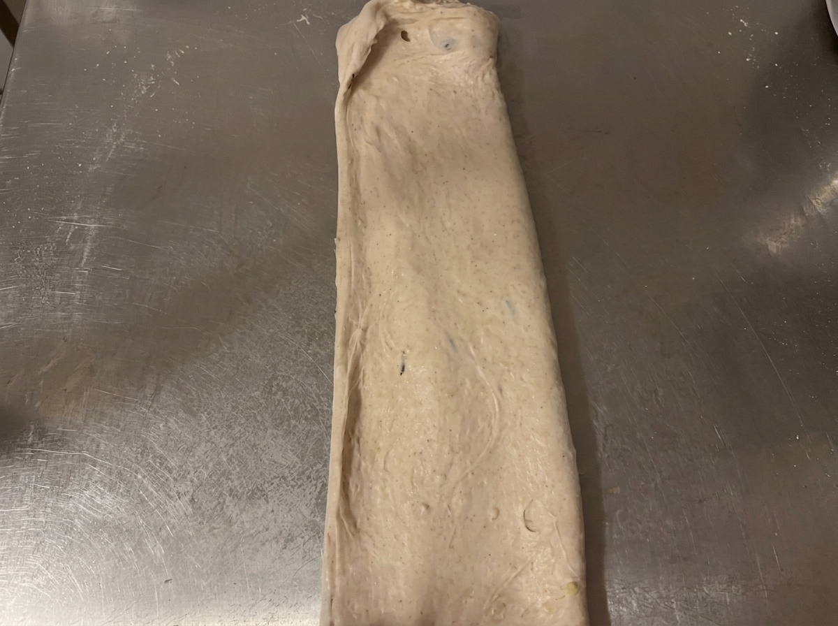 La masa cruda doblada en forma de paquete rectangular sobre la encimera de acero inoxidable.