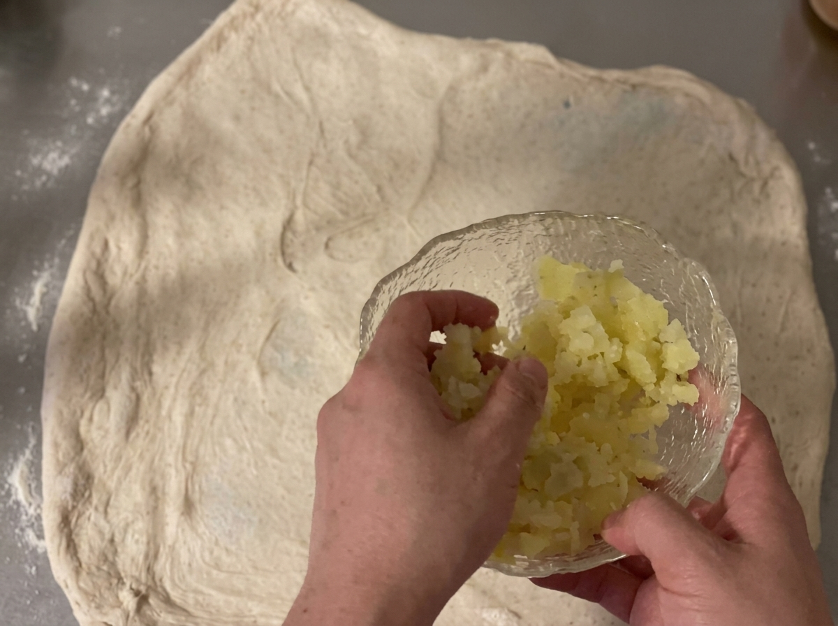 Dados de patata y queso cheddar rallado esparciéndose sobre una lámina de masa cruda.
