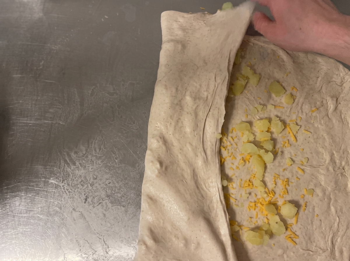 La masa enrollándose sobre la encimera para asegurar el relleno de queso y patata dentro.