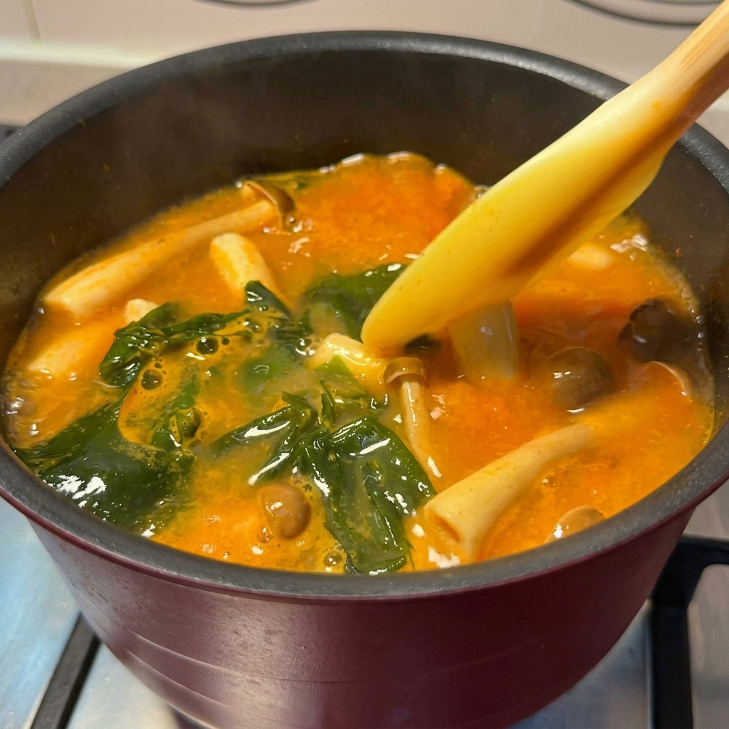Trozos de salmón dorado siendo añadidos a una olla de sopa de miso picante hirviendo a fuego lento.