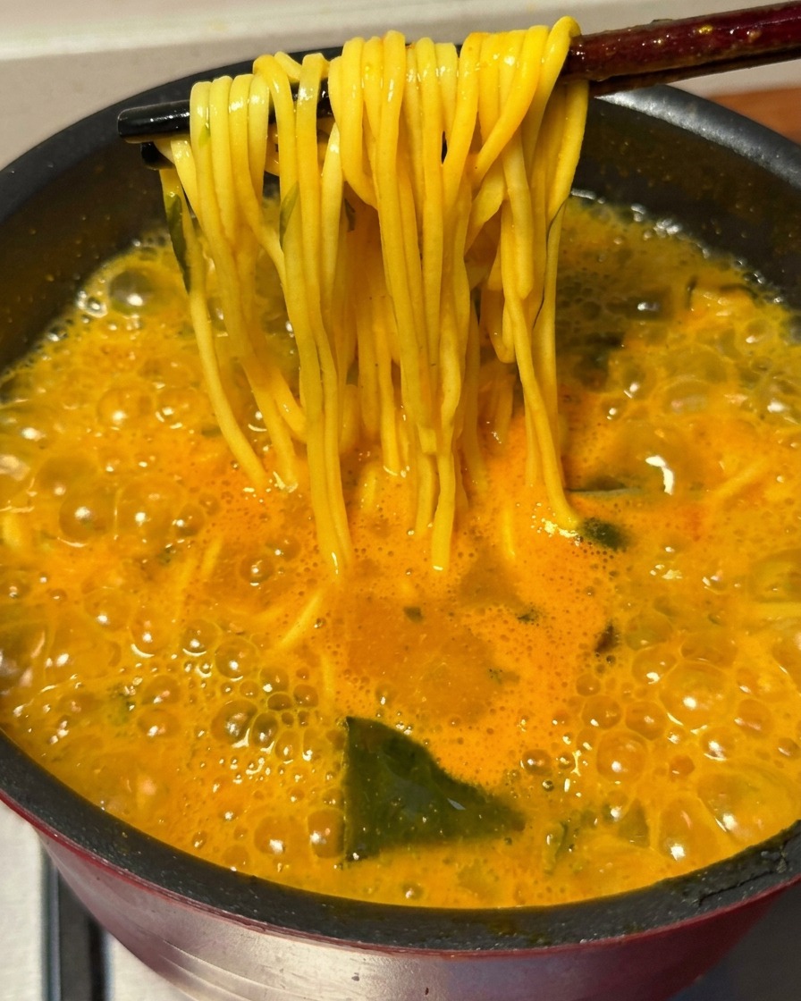 Un par de palillos levantando un manojo de fideos ramen cocidos dorados del caldo picante burbujeante.
