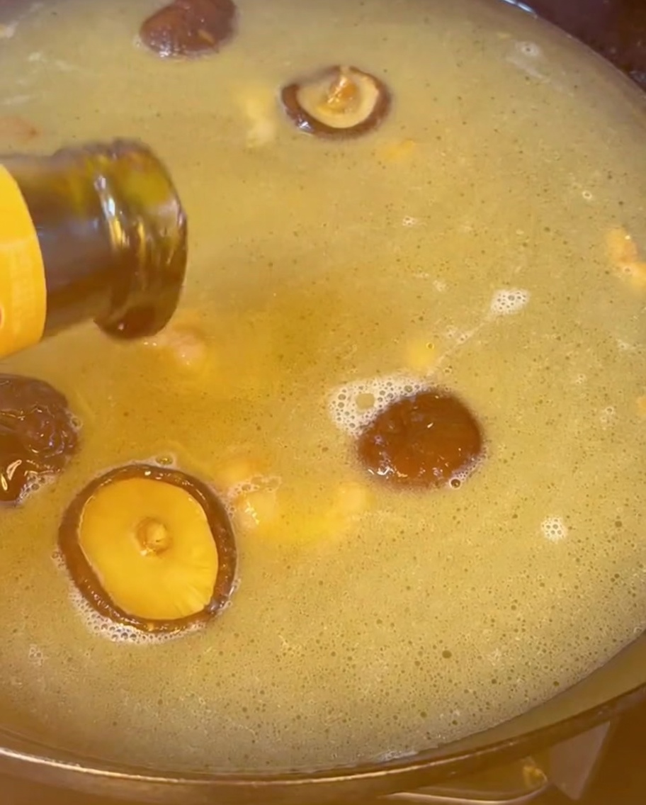 Salsa de ostras vertiéndose desde una botella en un caldo dorado e hirviendo lleno de setas shiitake.