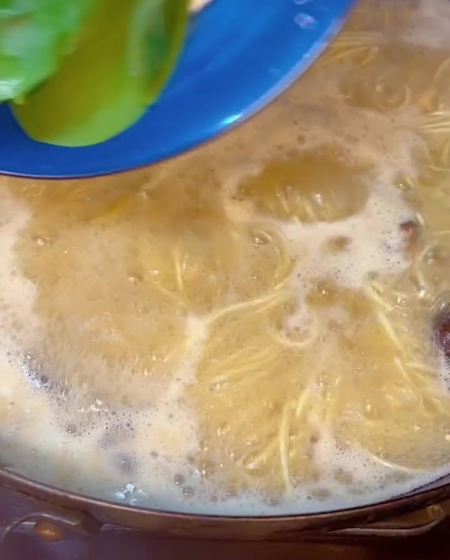 Bok choy verde y fresco sumergiéndose en una olla burbujeante de fideos de ramen y caldo.