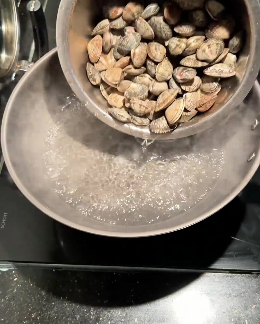 Almejas frescas siendo vertidas en una olla con agua hirviendo con sal.
