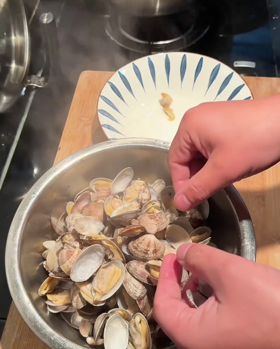 Manos quitando la carne de almeja de las conchas cocidas hacia un tazón.