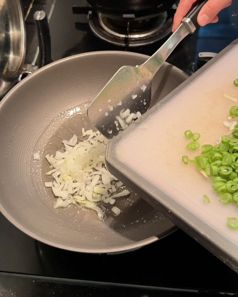 Cebollinas picadas y ejotes rebanados siendo salteados en un wok caliente con aceite.