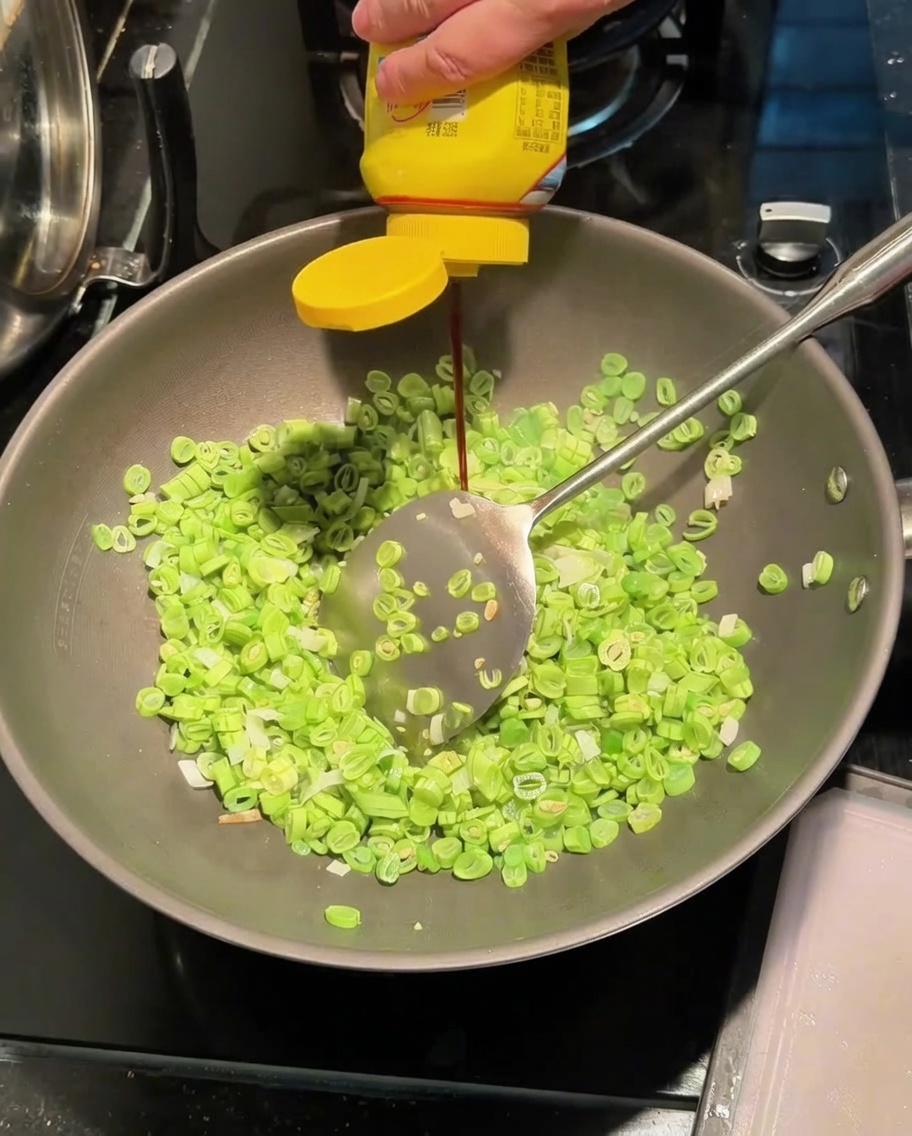 Agregando salsa sazonadora a un wok que contiene ejotes y cebollinas salteándose.