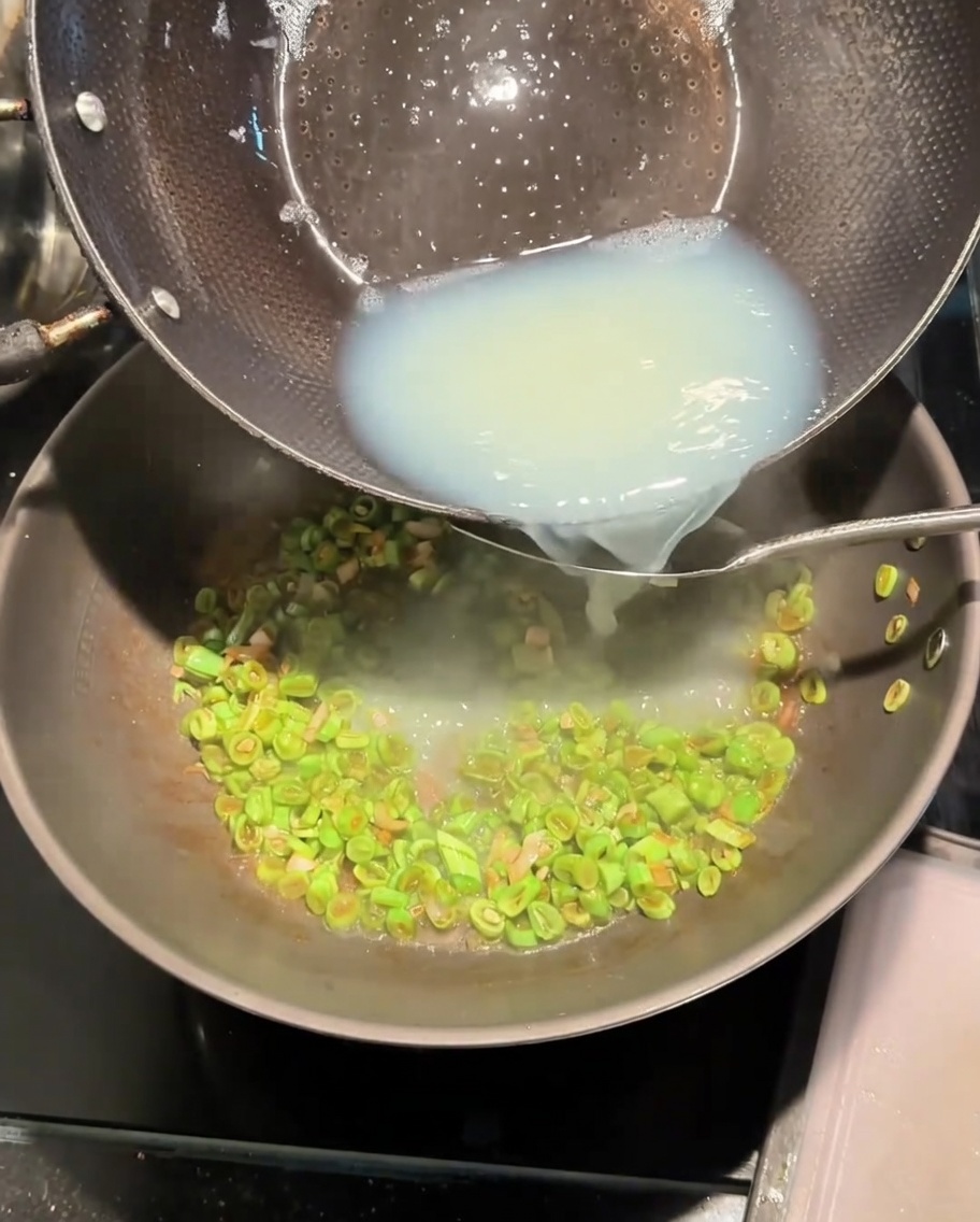Vertiendo el caldo blanco de almejas de una olla al wok con ejotes salteados.