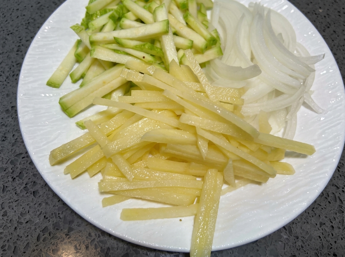 Tiras finas de calabacín, cebolla y papa sobre un plato blanco.