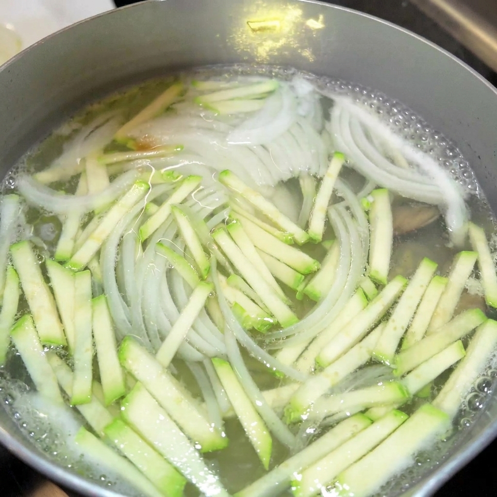 Primer plano de condimentos como salsa de soja y salsa de pescado siendo añadidos a una olla de caldo de verduras hirviendo.