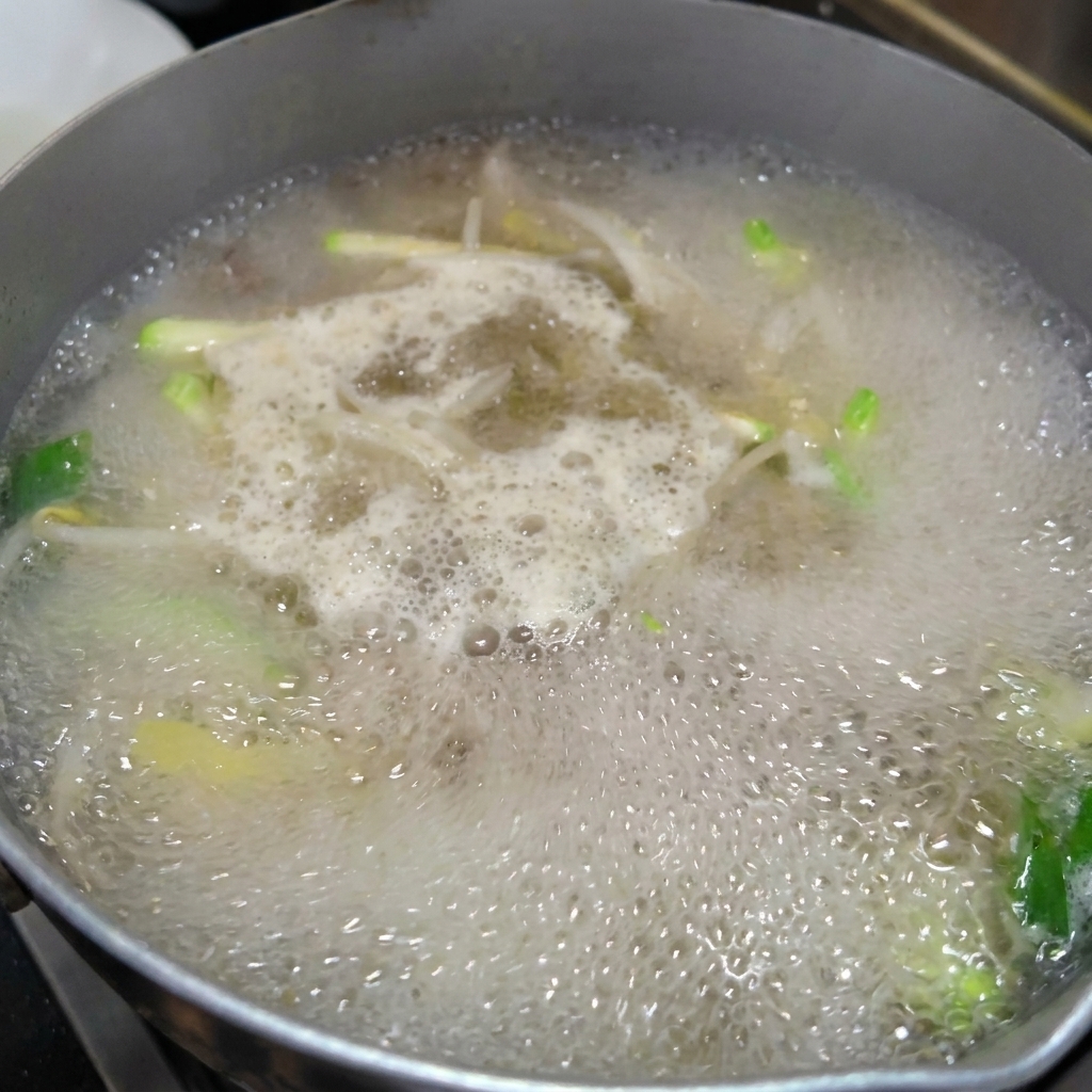 Fideos frescos hechos a mano siendo añadidos a una olla de caldo de verduras y almejas a fuego lento.