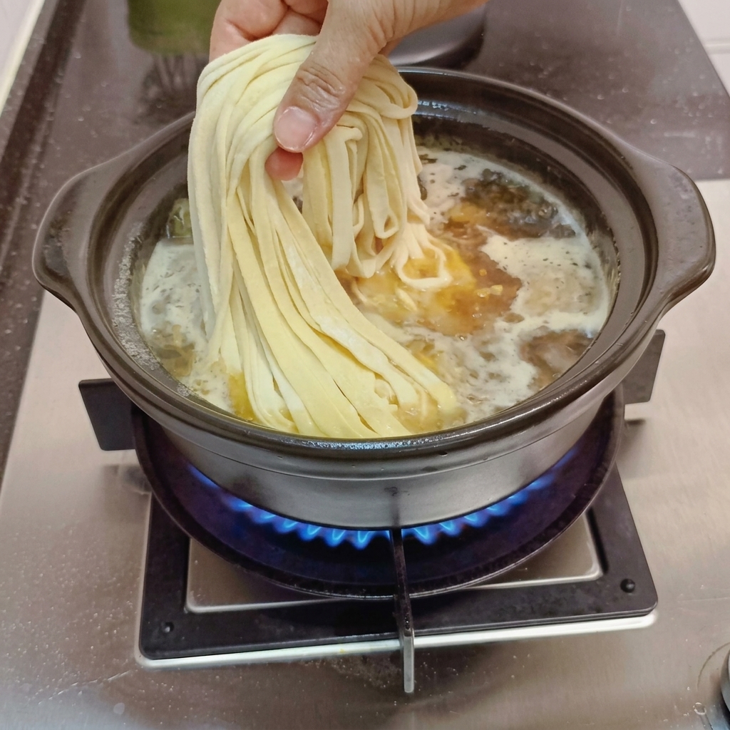 Fideos artesanales dejándose caer en el caldo a fuego lento.