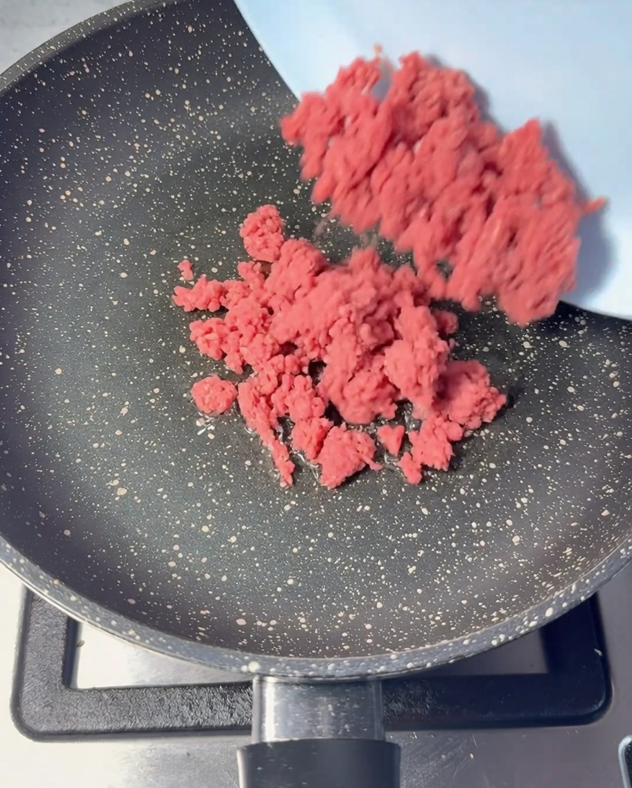 Carne picada de res cruda siendo añadida a una sartén con aceite.