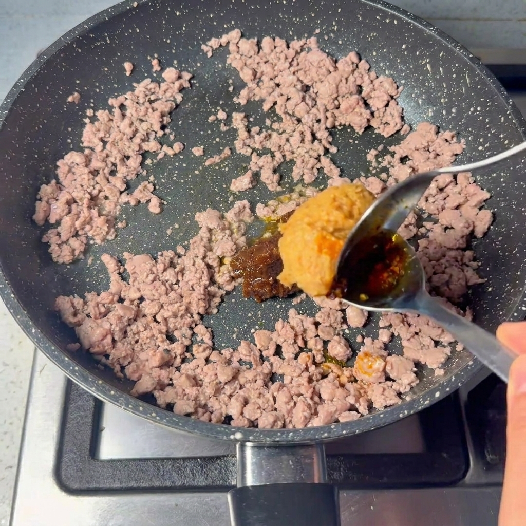 Una gran cucharada de pasta espesa siendo mezclada con la carne cocida.