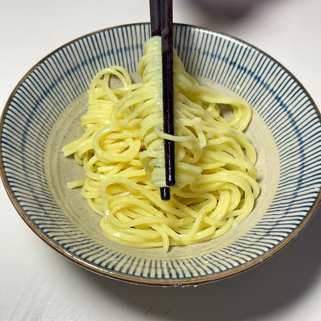 Fideos amarillos cocidos siendo puestos en un tazón de cerámica.
