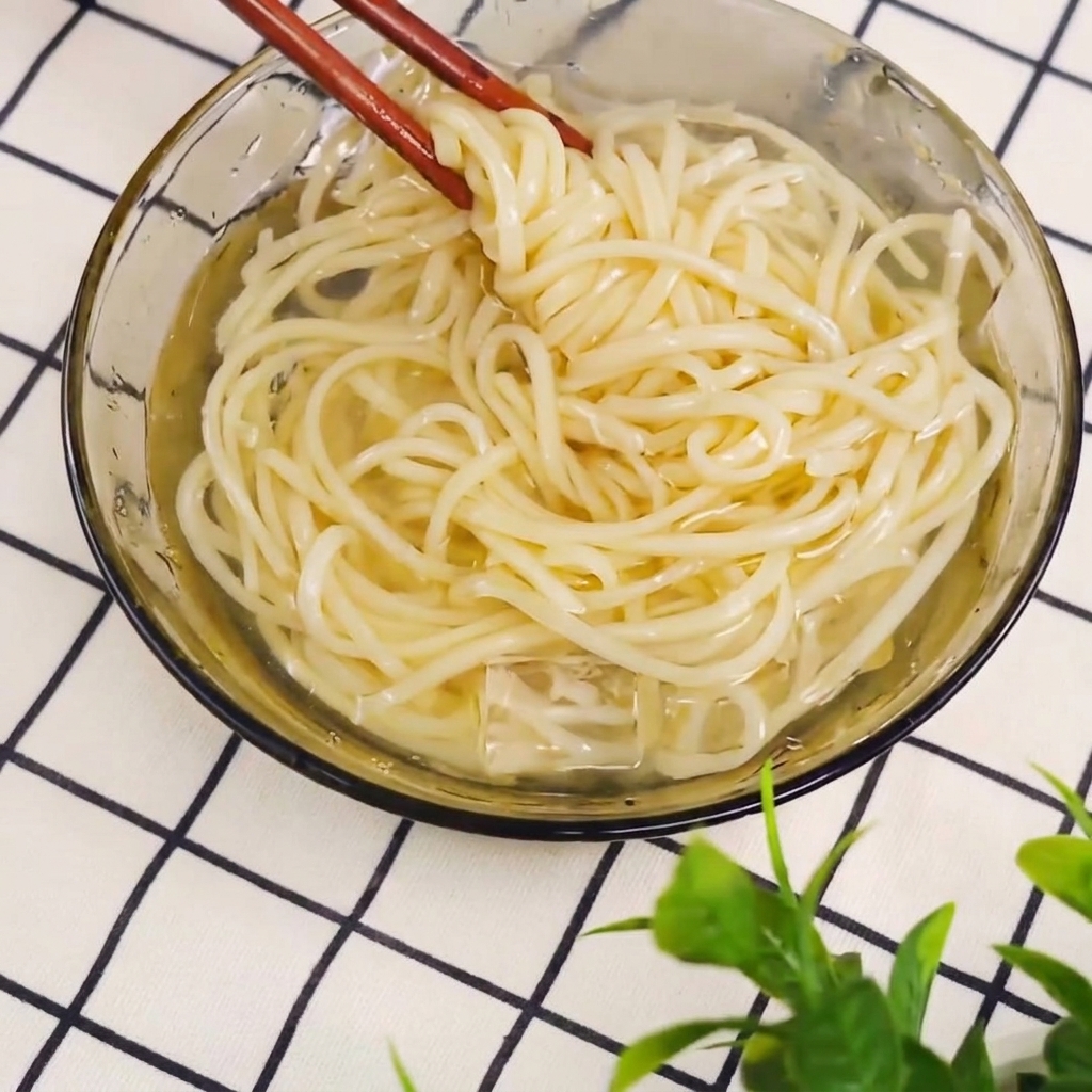 Fideos cocidos siendo sacados de una olla con palillos.
