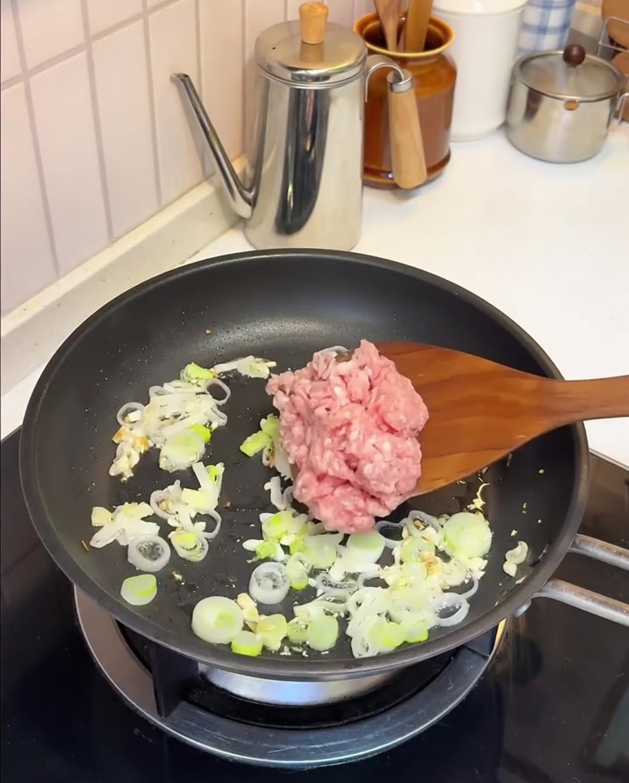 Carne de cerdo picada salteándose en una sartén con ajo y cebolleta.