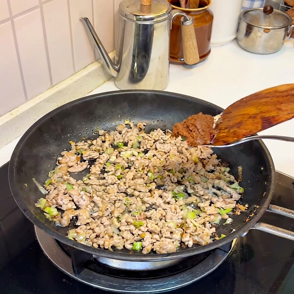 Pasta de miso añadiéndose a la carne cocinada en la sartén.