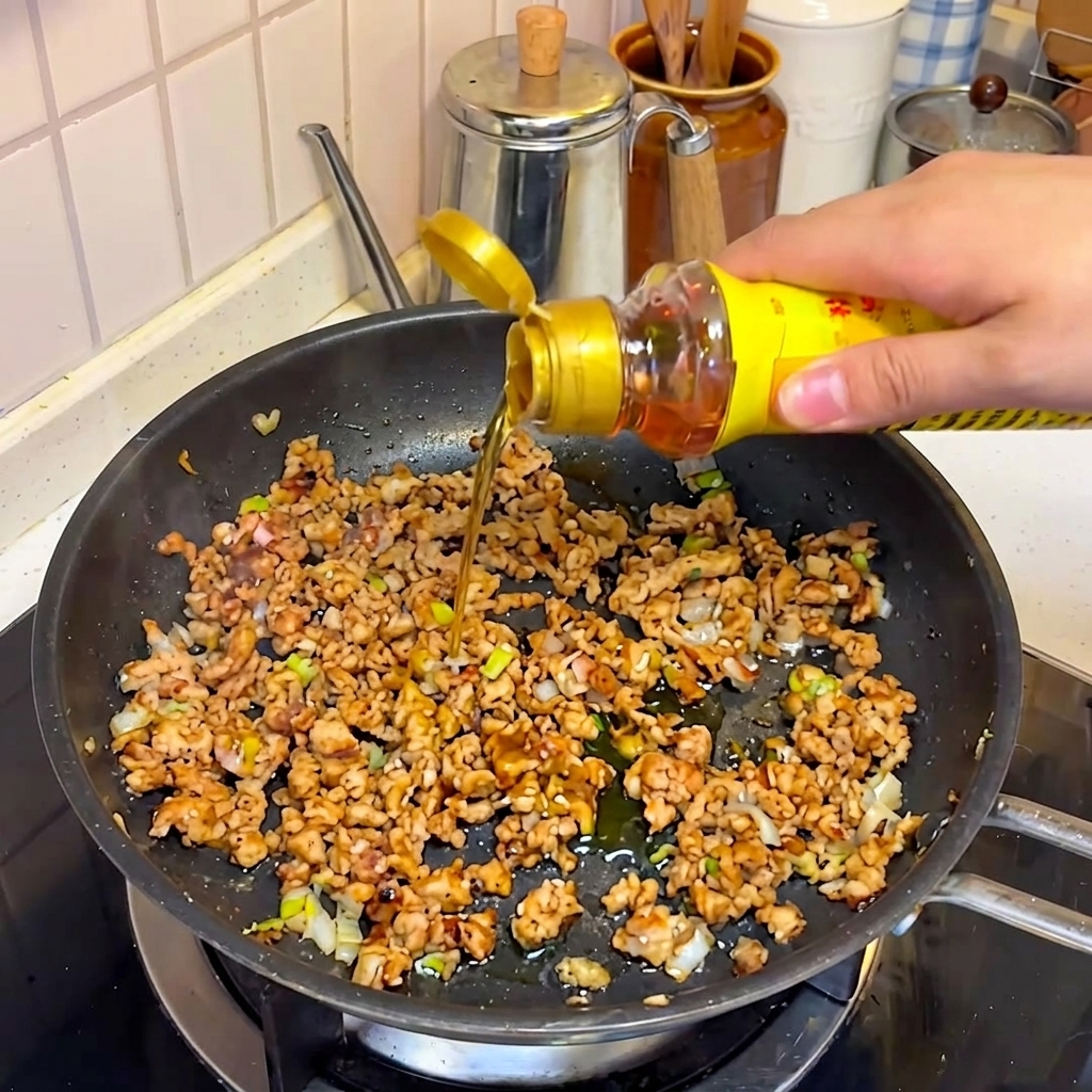 Aceite de sésamo y otros condimentos vertiéndose sobre la mezcla de carne sazonada.