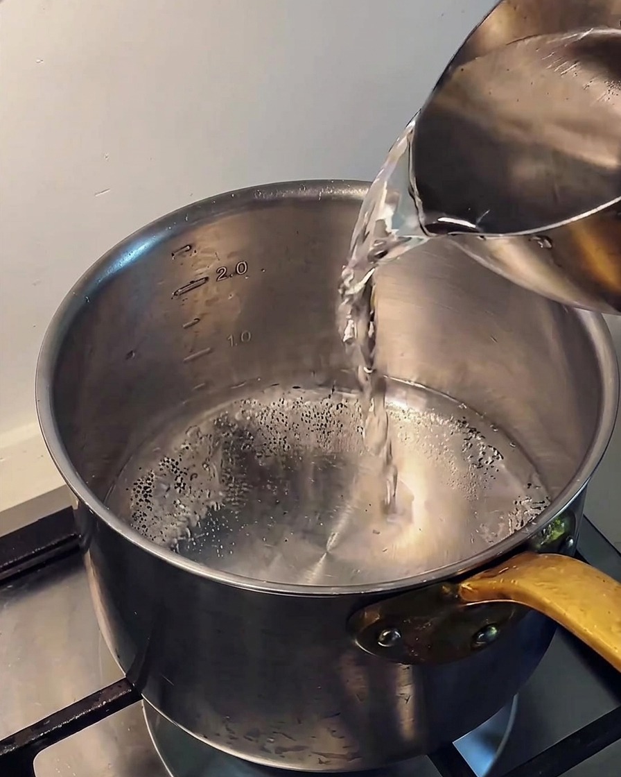 Verter agua fría de una jarra de metal en una olla de acero inoxidable sobre la estufa.