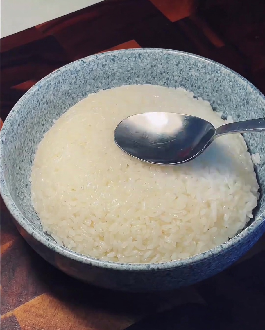 Una cuchara de metal presionando el centro de una montaña de arroz blanco esponjoso en un cuenco de cerámica.