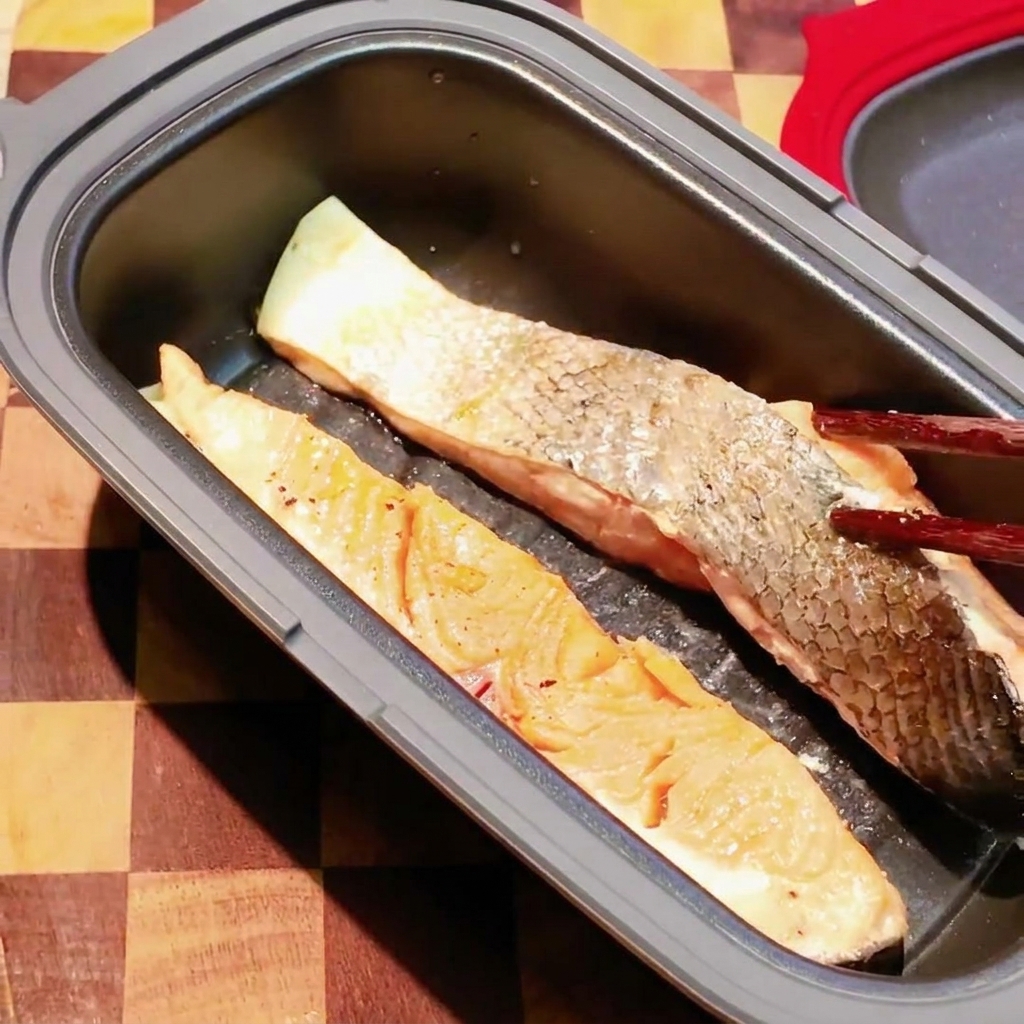 Palillos dando la vuelta a un filete de salmón parcialmente cocinado en una sartén oscura de microondas.