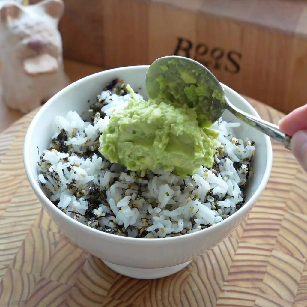 Una capa de aguacate machacado extendida suavemente sobre la base de arroz en un bol.