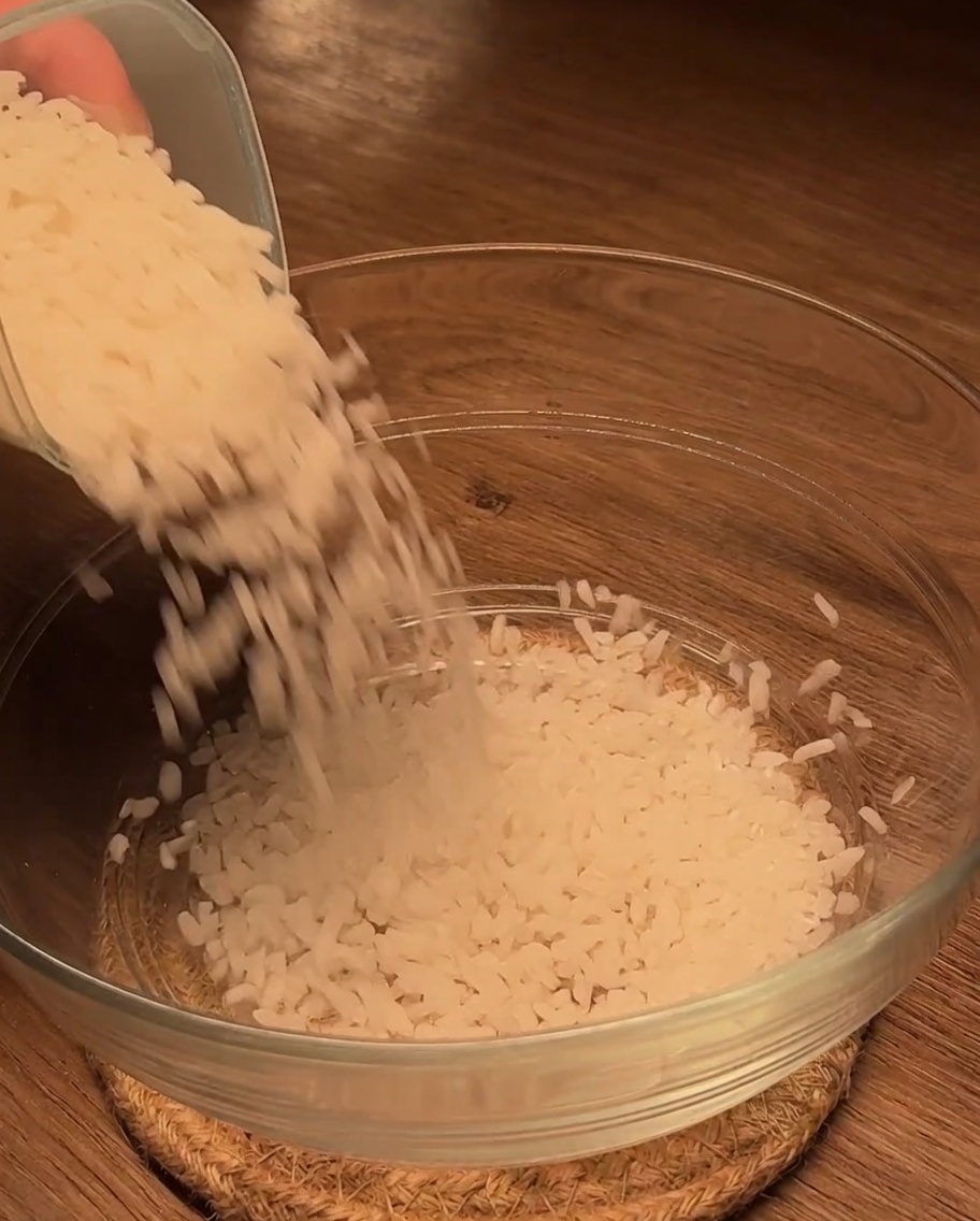 Arroz blanco crudo vertido en un cuenco de cristal sobre una superficie de madera.