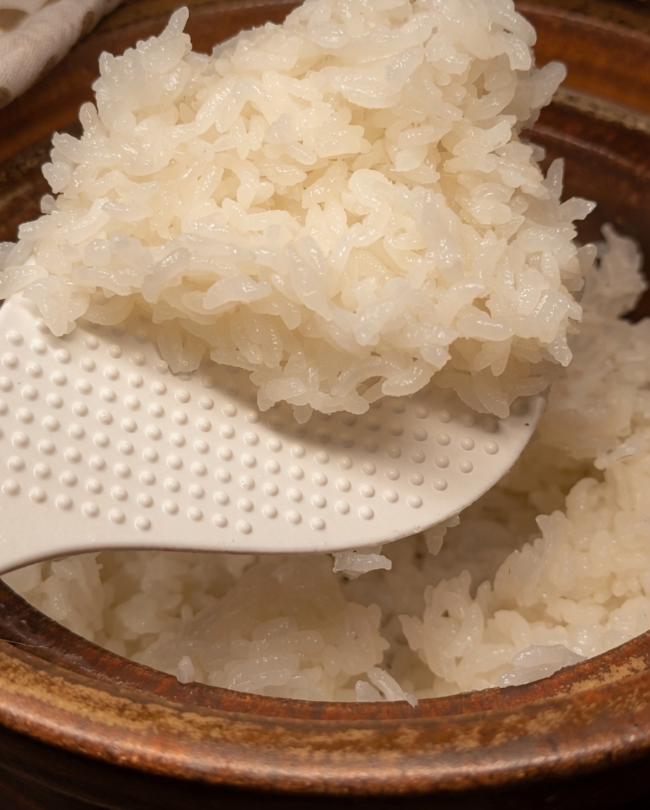 Una vista de primer plano de arroz blanco cocido en una olla de barro mezclado suavemente con el condimento usando una paleta de arroz blanca.