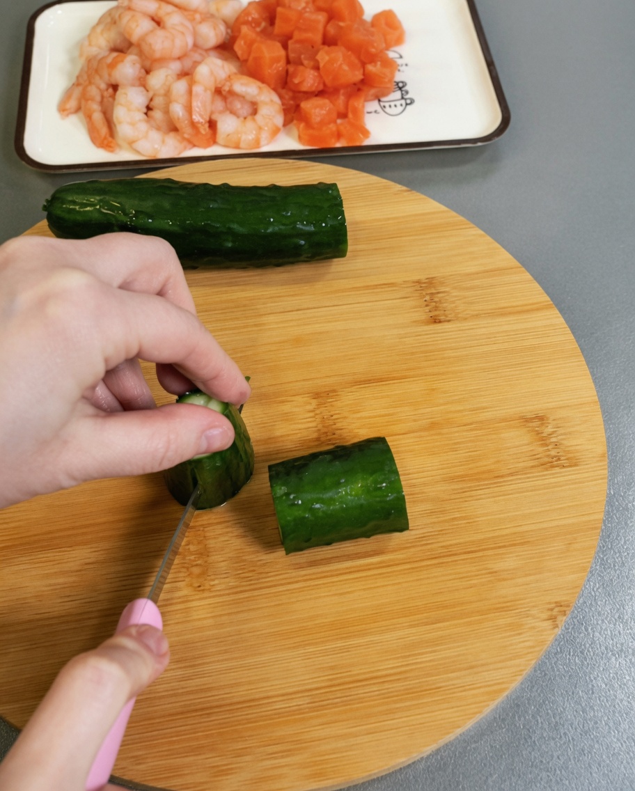Pepino verde fresco siendo picado en cubos pequeños sobre una superficie de madera.